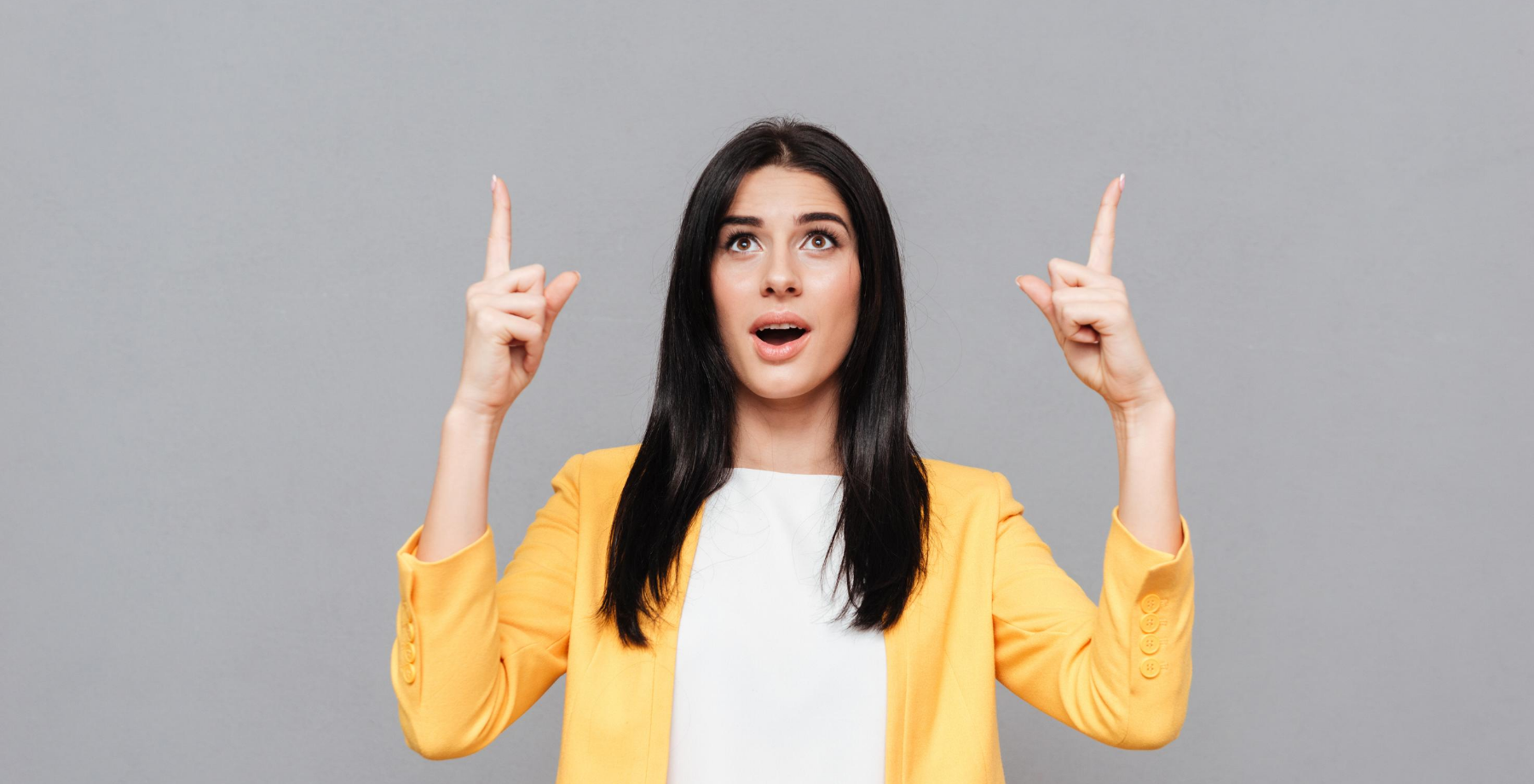 Woman in yellow blazer pointing upward with both hands symbolising professional growth